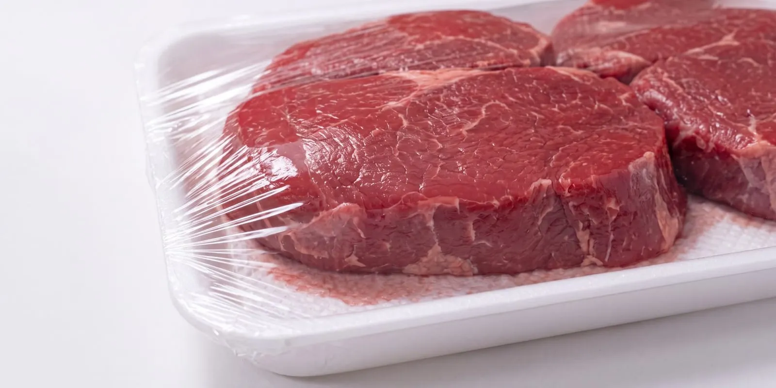 A soaked absorbent pad under raw beef in a conventional tray, purge pooling around it