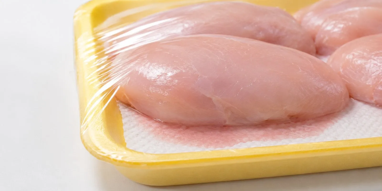 Hands peeling a soaked pad off the bottom of a chicken tray
