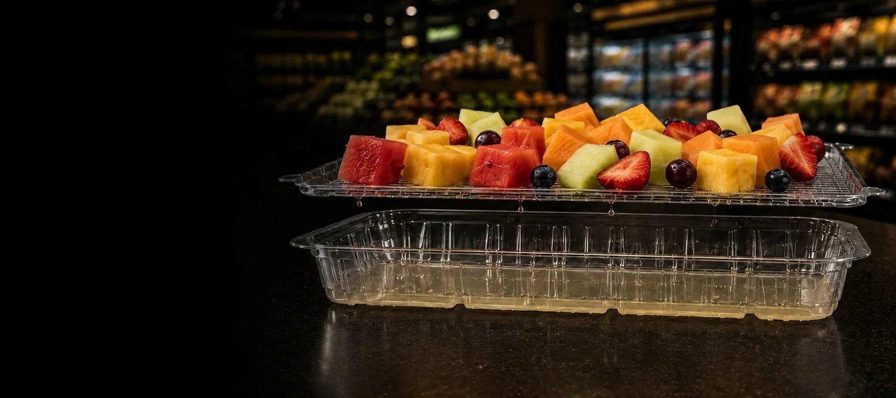 Lucid Infinity two-piece tray: cut fruit resting above on the elevated rack, released juice dripping into the sealed reservoir below
